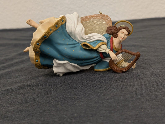 Resin Christmas ornament of a flying angel in a blue starry dress playing a brown harp.
