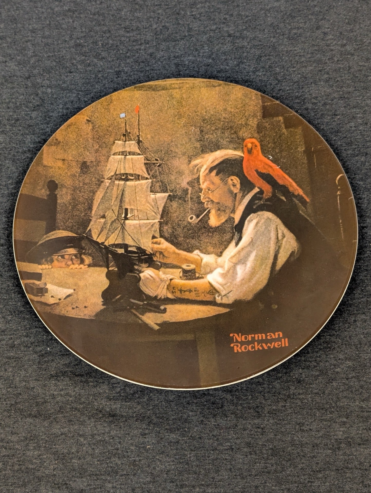 Round collector plate depicting an old man building a model ship with a red parrot on his shoulder.