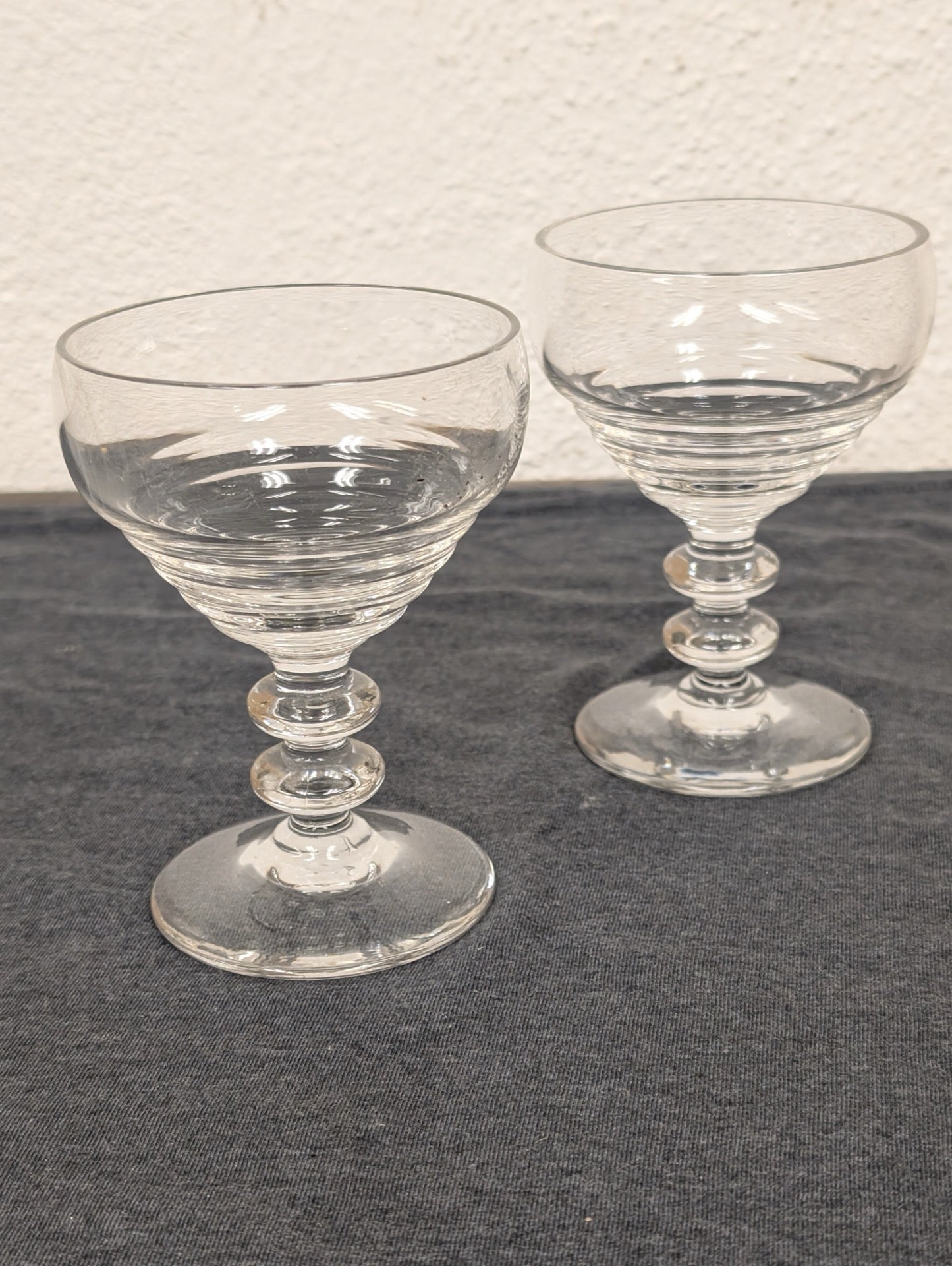Two clear glass coupe glasses with ribbed bowls and double-ball stems on a gray background.
