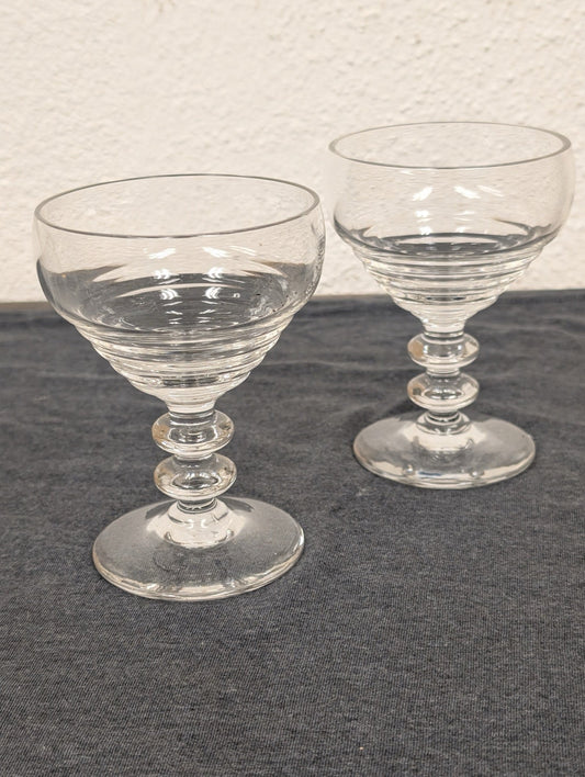 Two clear glass coupe glasses with ribbed bowls and double-ball stems on a gray background.