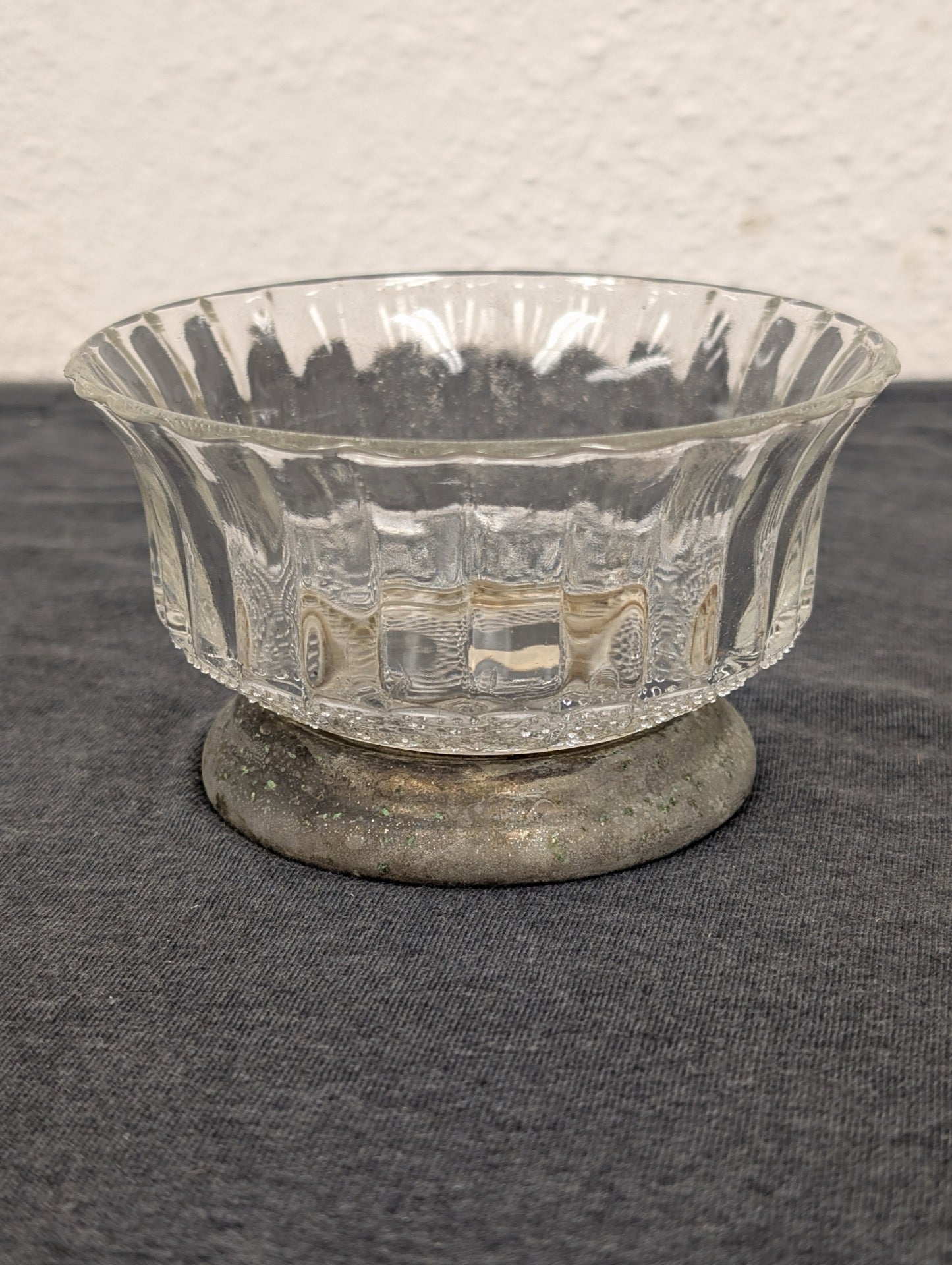 Clear fluted glass bowl resting on a low, tarnished metal circular base.