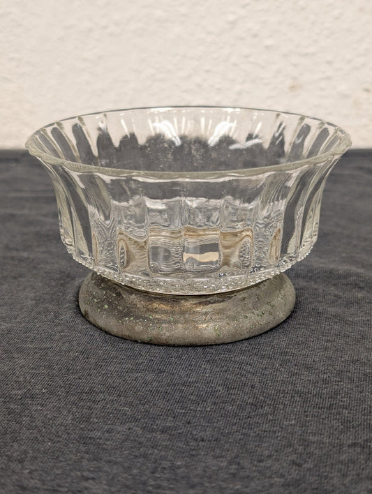 Clear fluted glass bowl resting on a low, tarnished metal circular base.