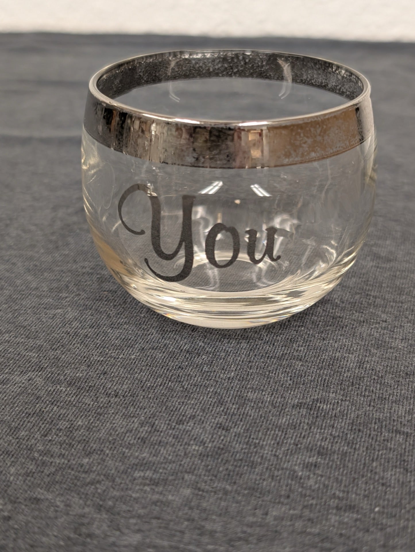 Clear lowball glass with a silver rim and the word 'You' printed in gray script.
