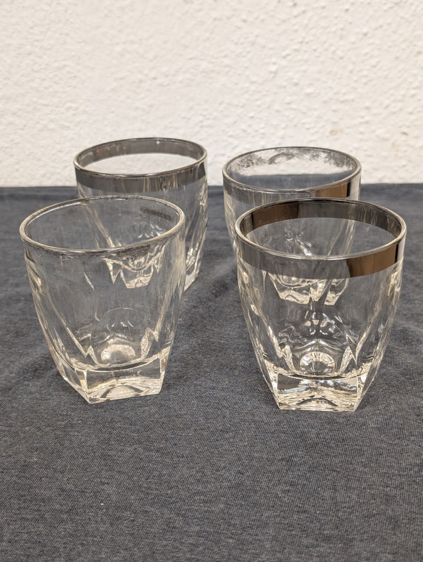 Four clear glass lowball glasses with silver rims and heavy faceted bases.