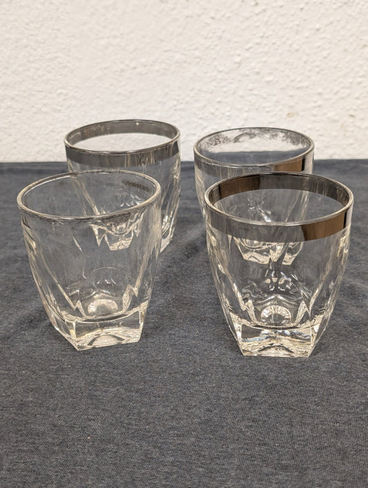 Four clear glass lowball glasses with silver rims and heavy faceted bases.