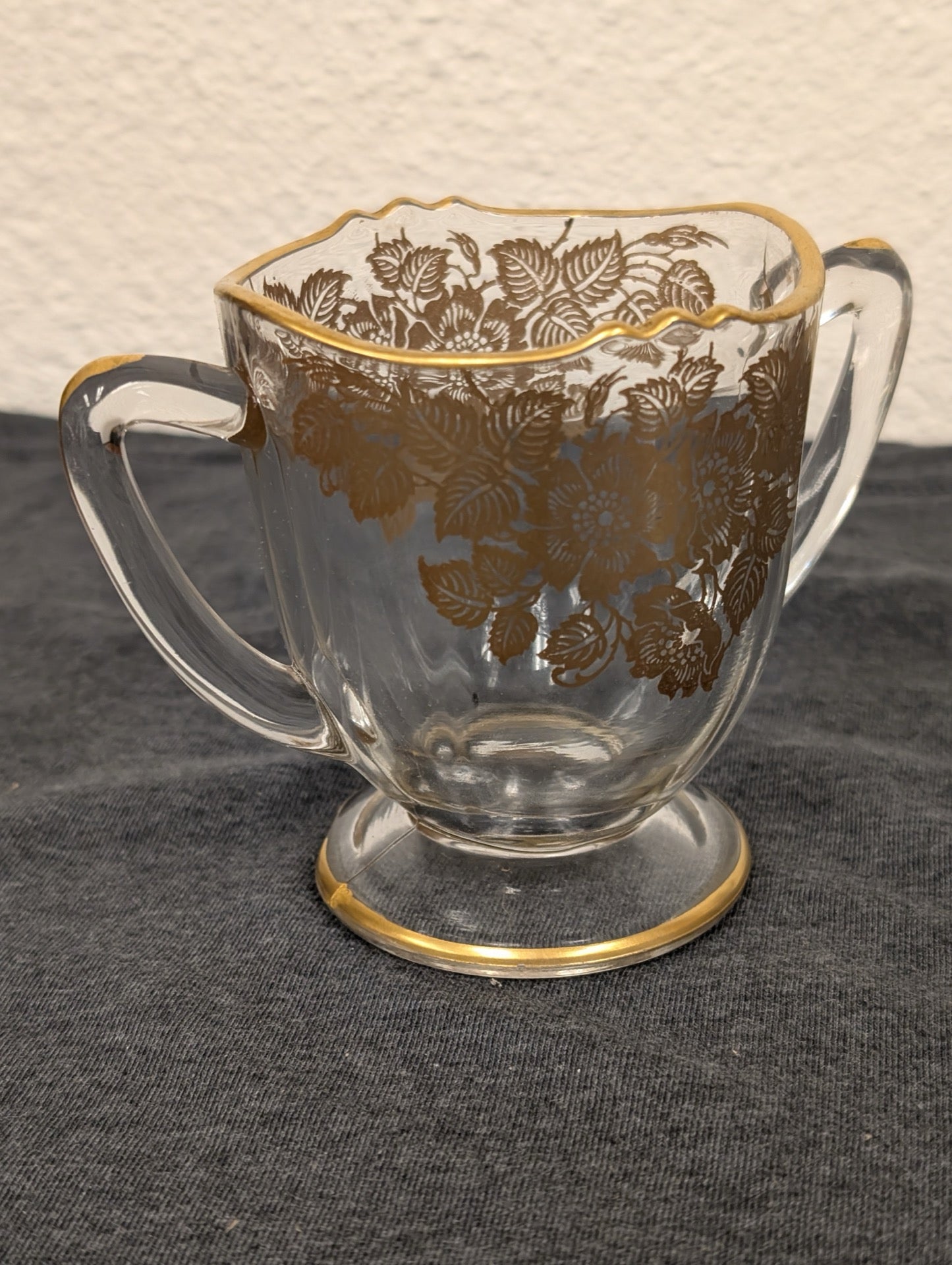 Clear glass sugar bowl with two handles, a scalloped edge, and a gold floral pattern.