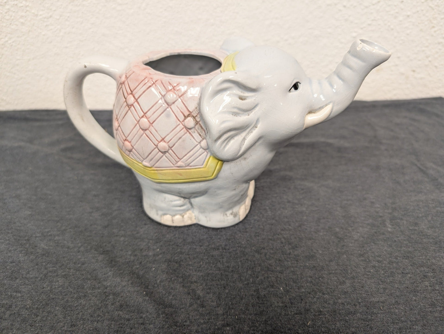 Light blue ceramic elephant shaped pitcher with a pink patterned blanket and trunk acting as a spout.