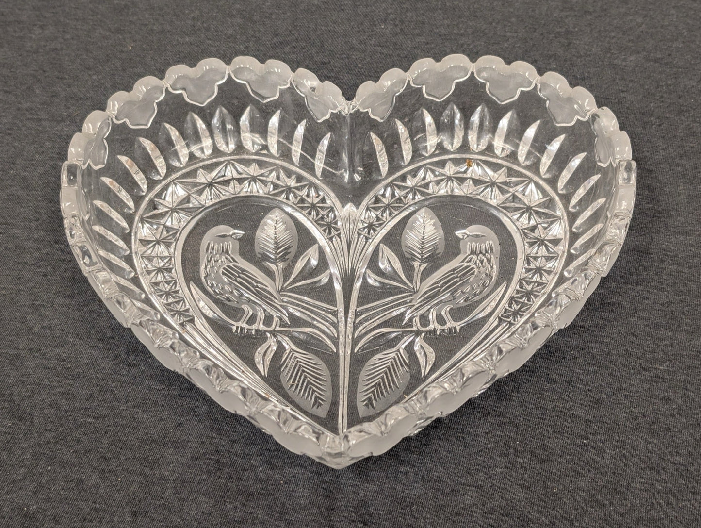 Clear vintage pressed glass heart-shaped bowl featuring an embossed bird and leaf design.