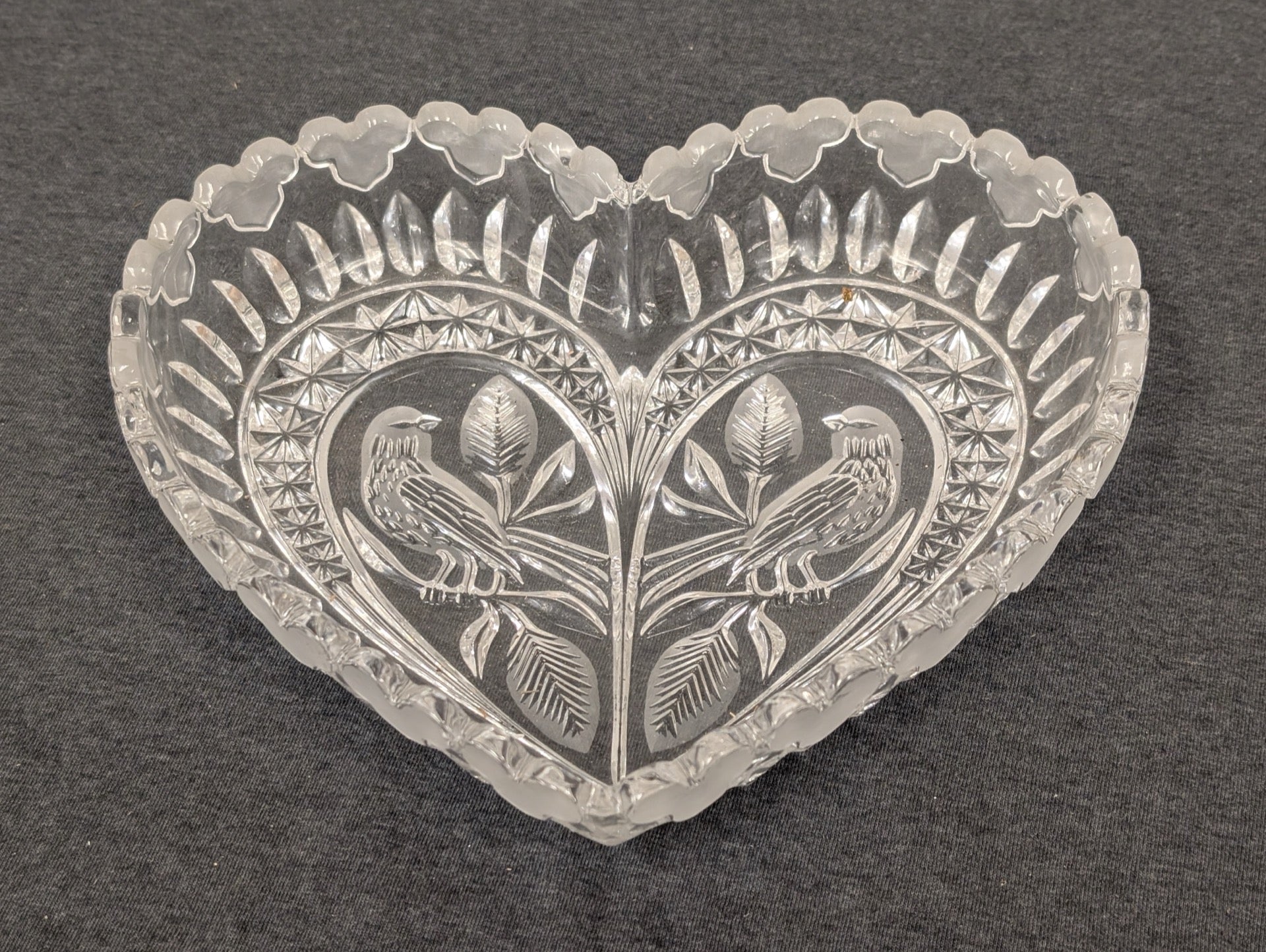 Clear vintage pressed glass heart-shaped bowl featuring an embossed bird and leaf design.