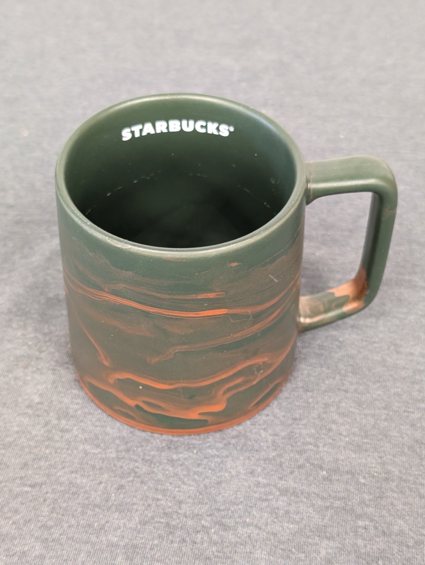 Starbucks coffee mug with a matte green finish and copper colored swirls.