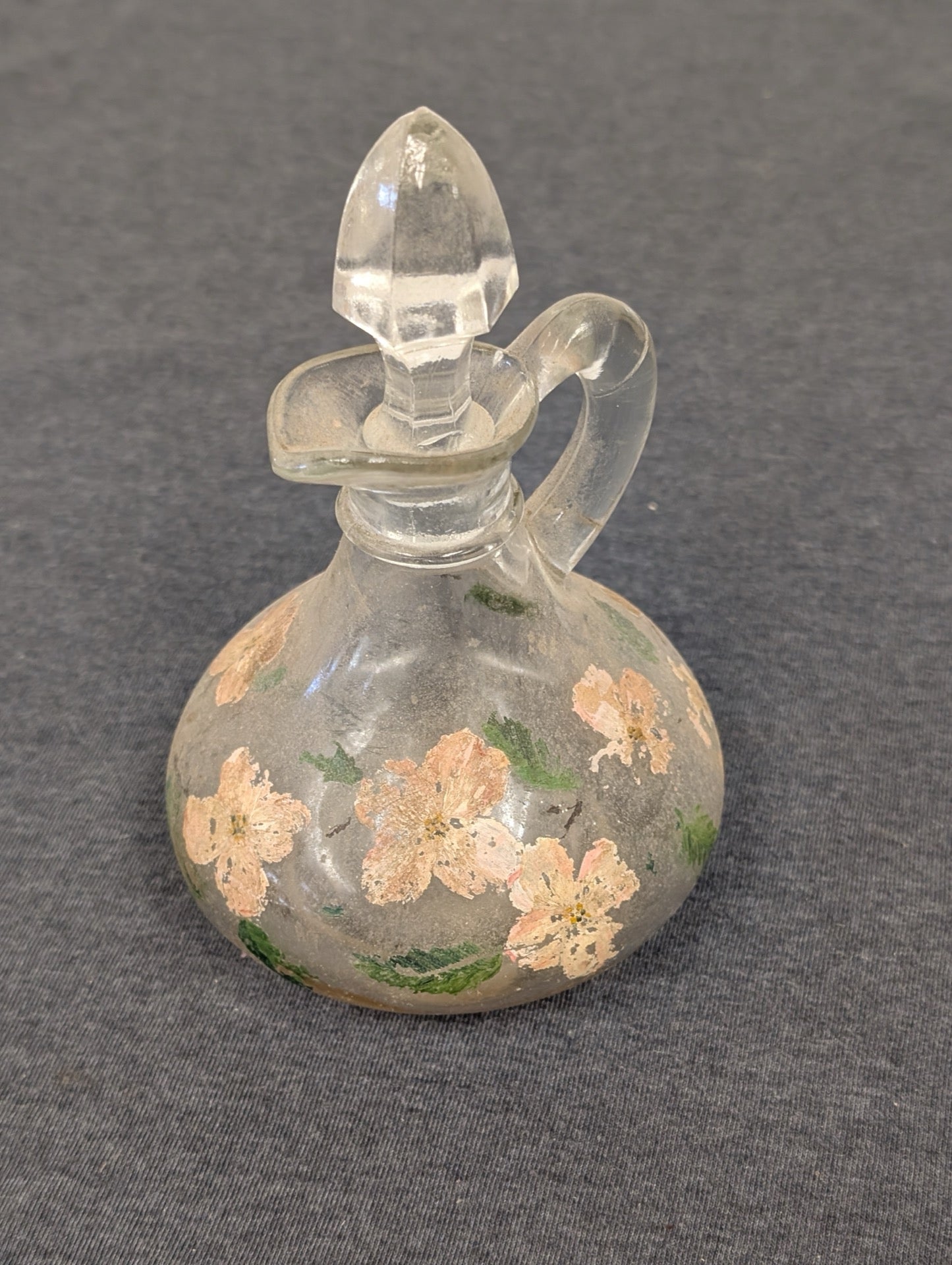 Small clear glass cruet painted with pink flowers, featuring a handle and faceted stopper.