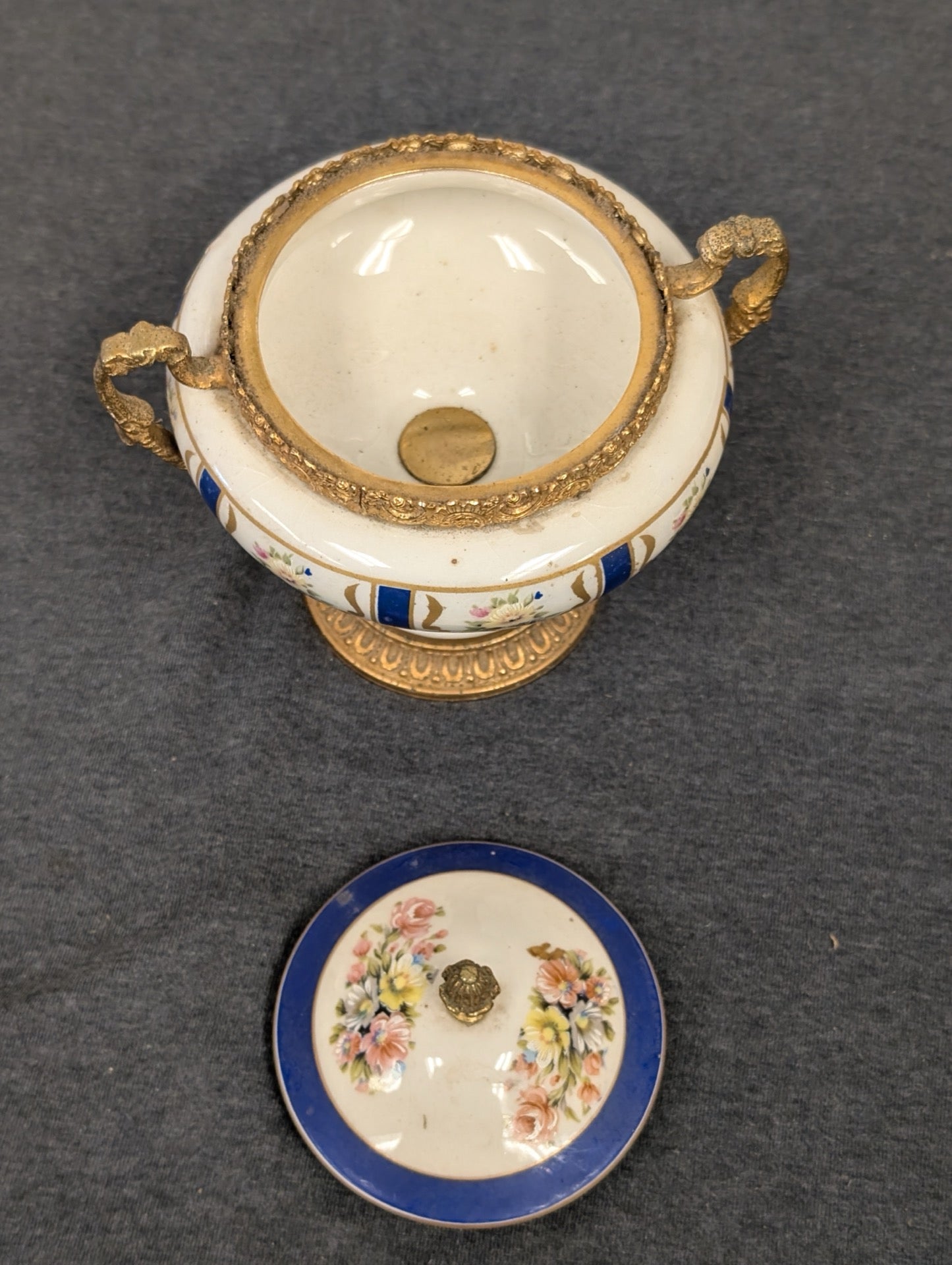 Top view of an open porcelain and brass urn with a floral lid set aside.
