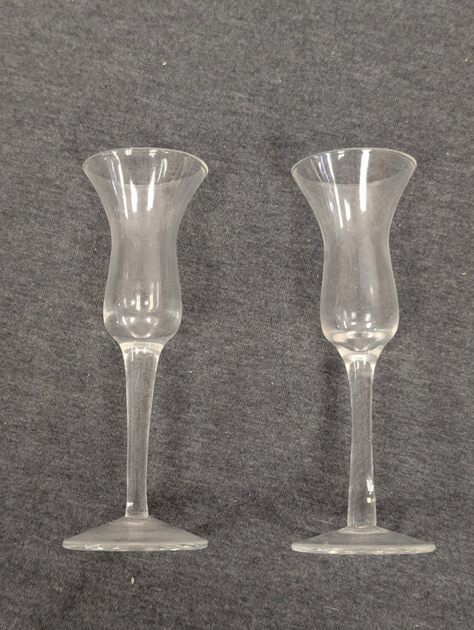 Two clear glass cordials with tall stems and flared rims.