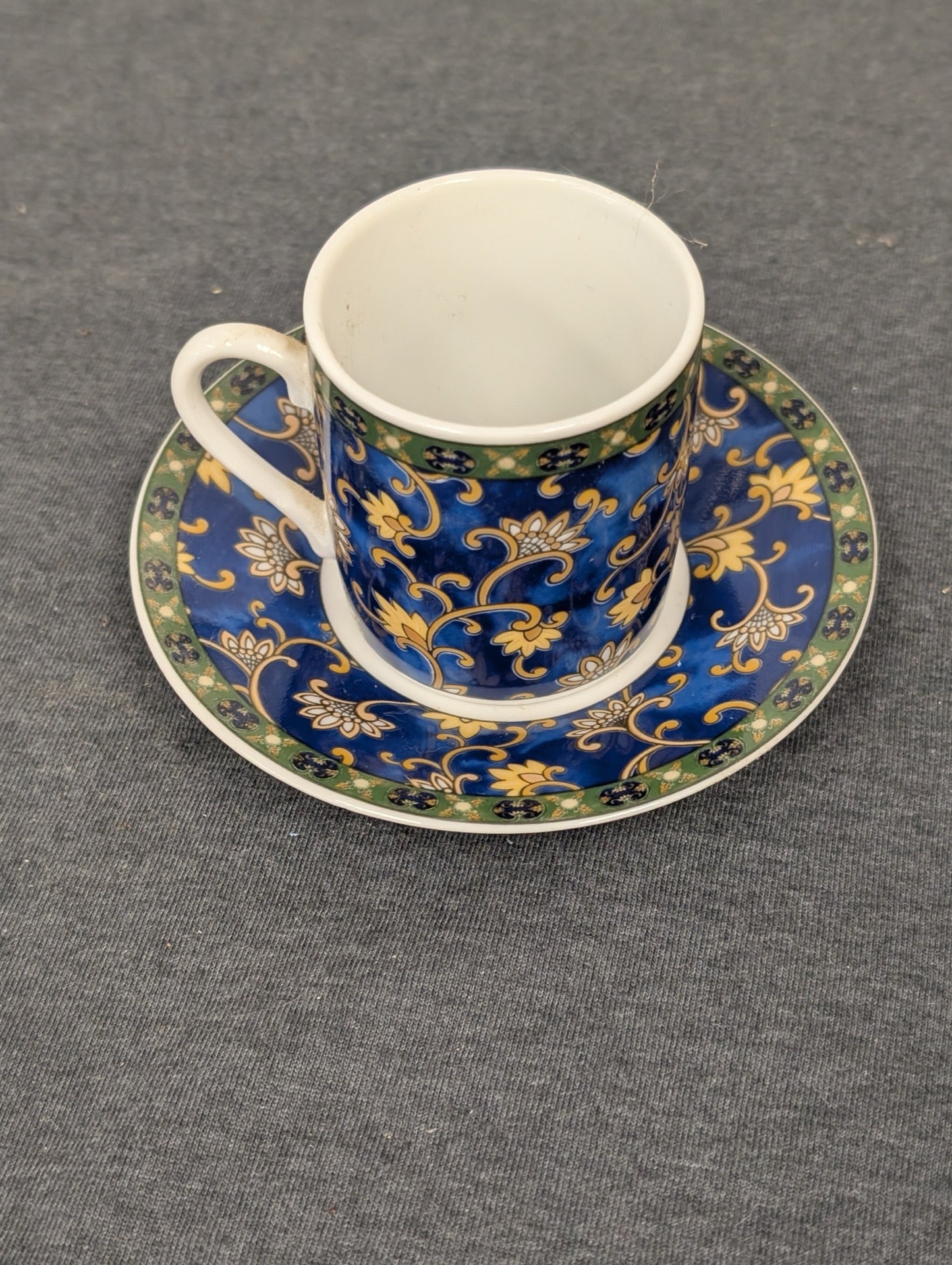 Blue espresso cup with yellow floral patterns sitting on a matching saucer.