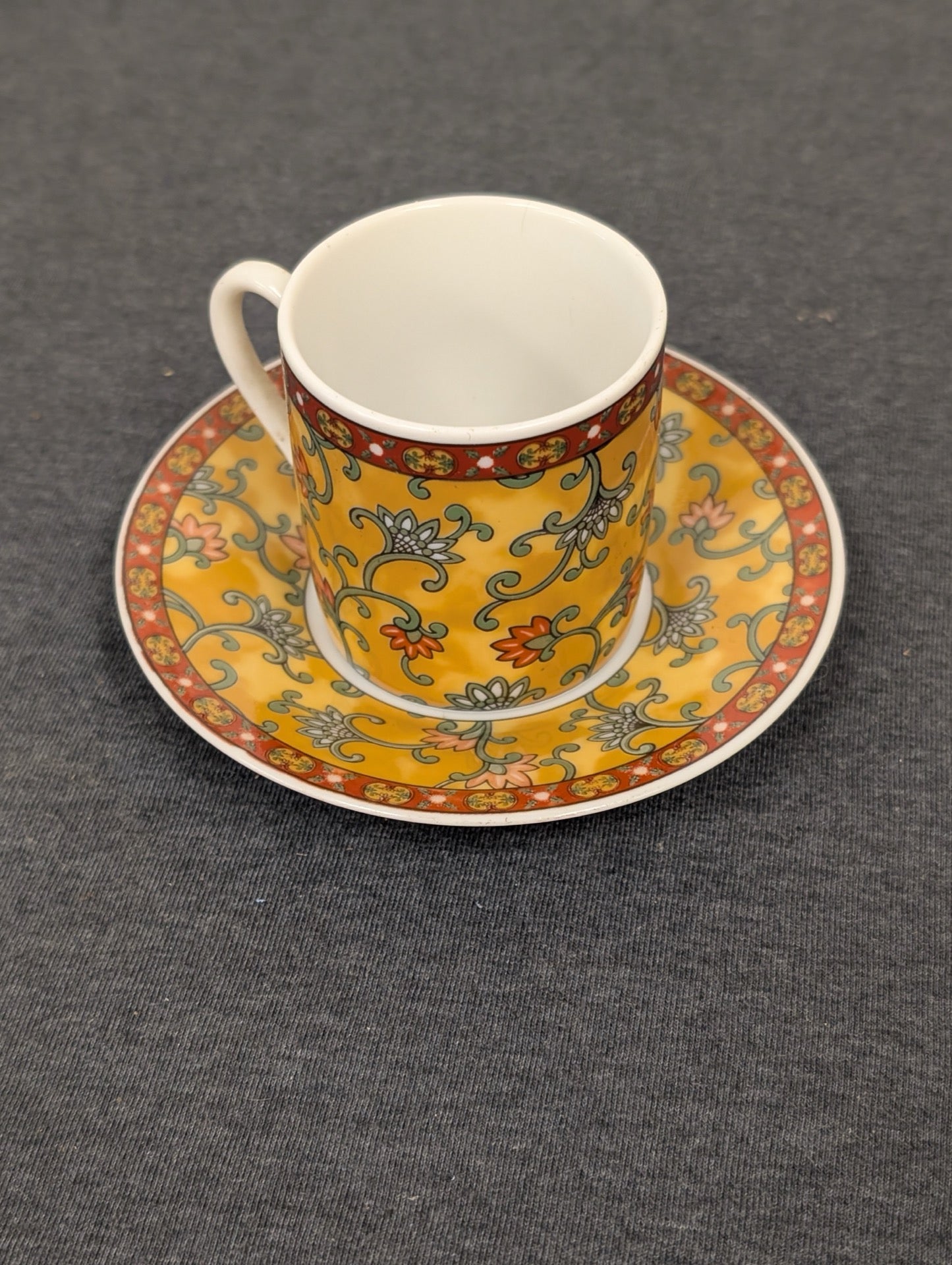 Yellow espresso cup with floral patterns sitting on a matching saucer.