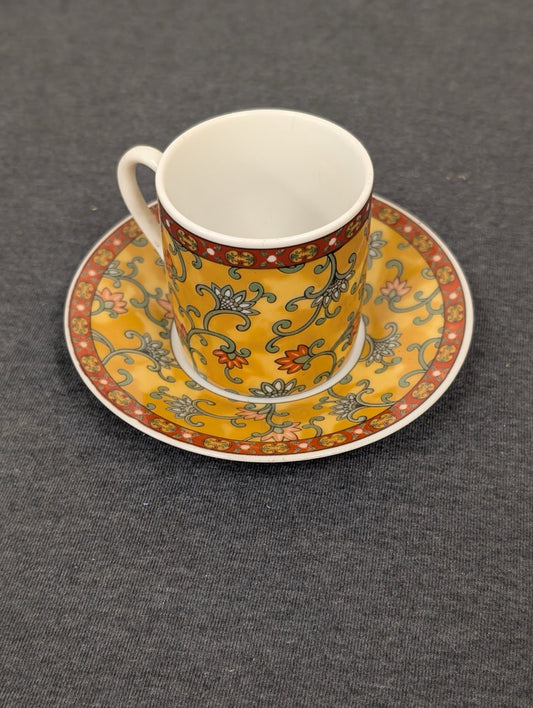 Yellow espresso cup with floral patterns sitting on a matching saucer.