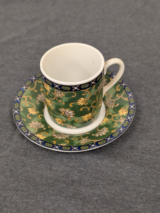 Green espresso cup with yellow floral patterns sitting on a matching saucer.