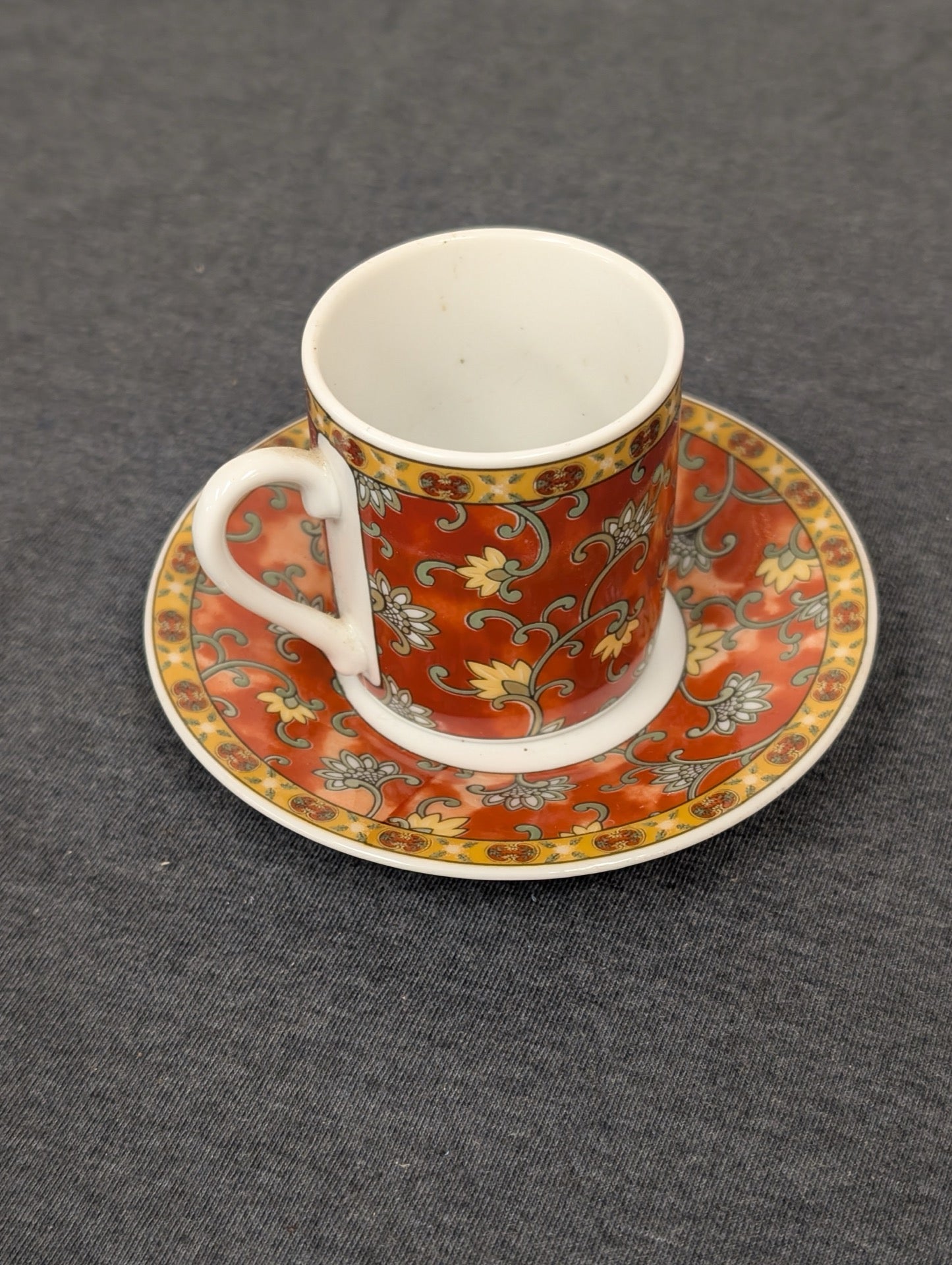 Red espresso cup with floral patterns sitting on a matching saucer.
