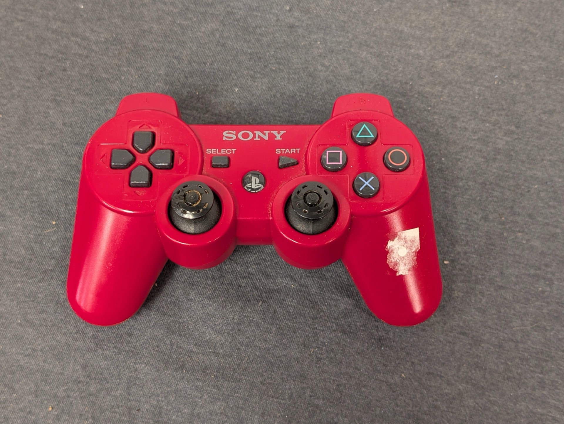 Red Sony PS3 DualShock 3 controller showing worn thumbsticks