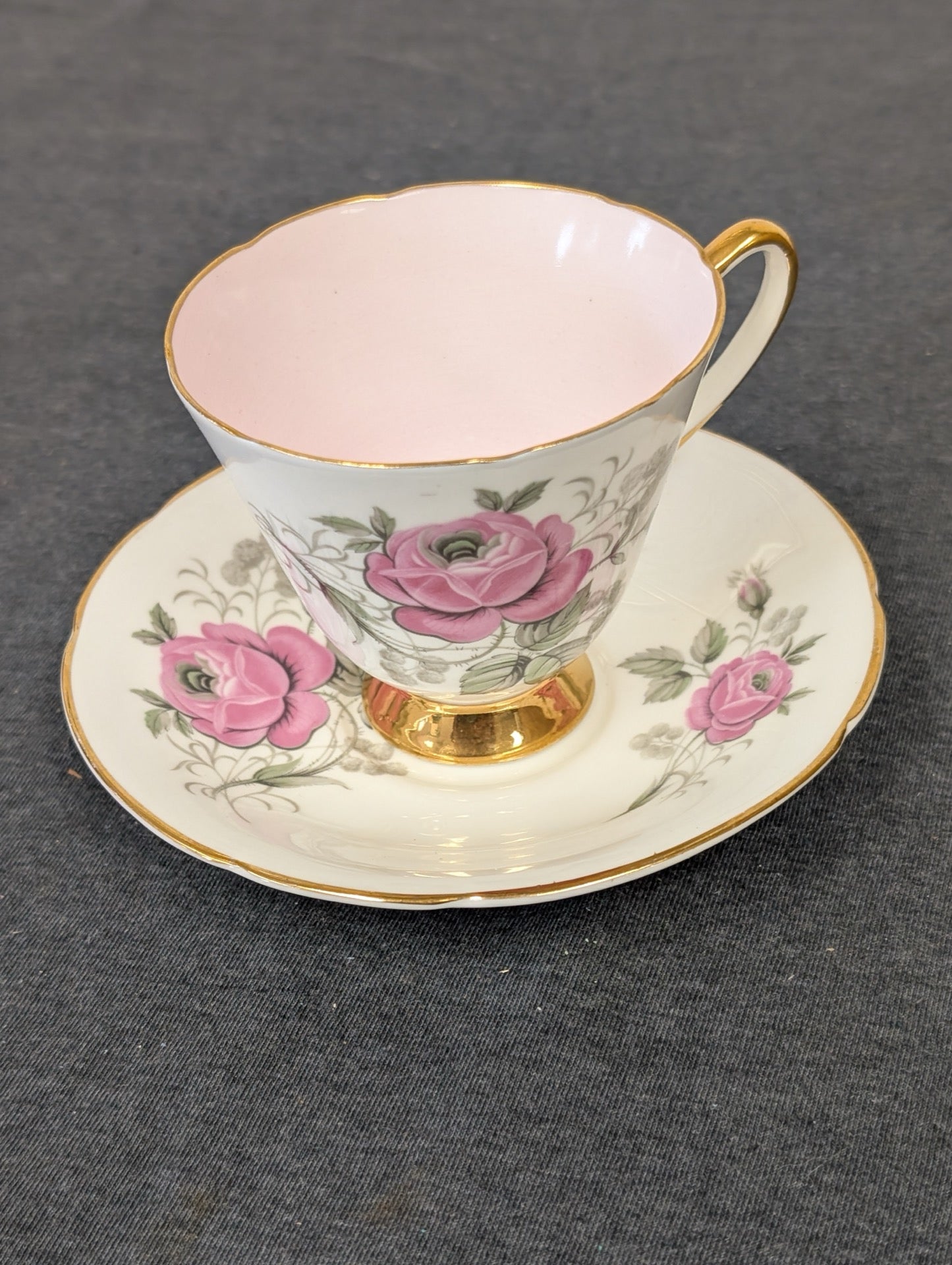 Vintage Old Royal bone china teacup and saucer featuring large pink roses and gold trim against a white background.