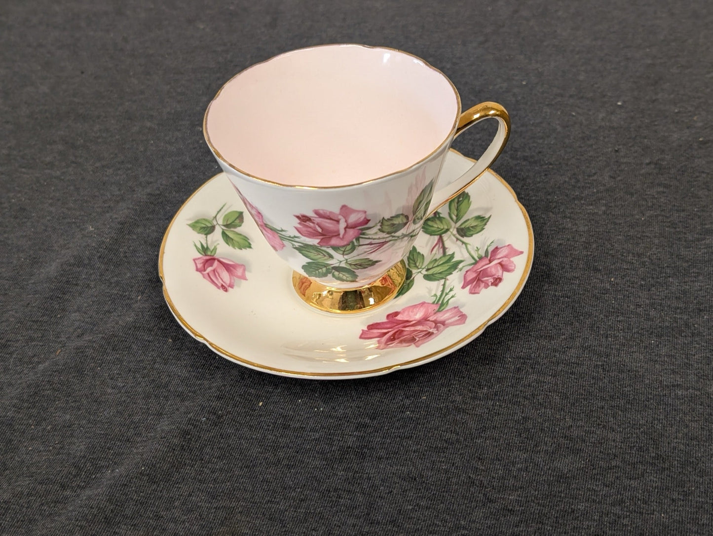 Angled view of a vintage Old Royal teacup and saucer featuring pink rose illustrations and a golden footed base.
