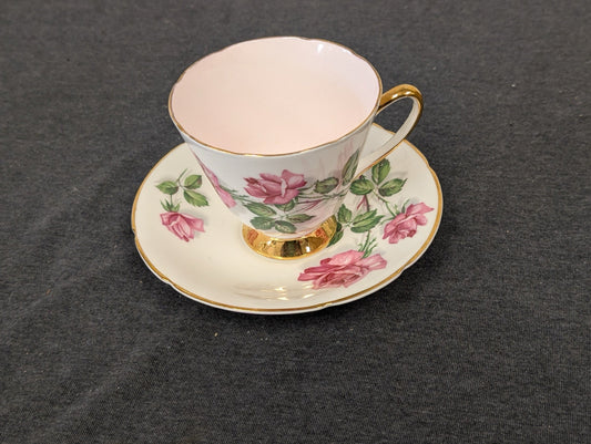 Angled view of a vintage Old Royal teacup and saucer featuring pink rose illustrations and a golden footed base.