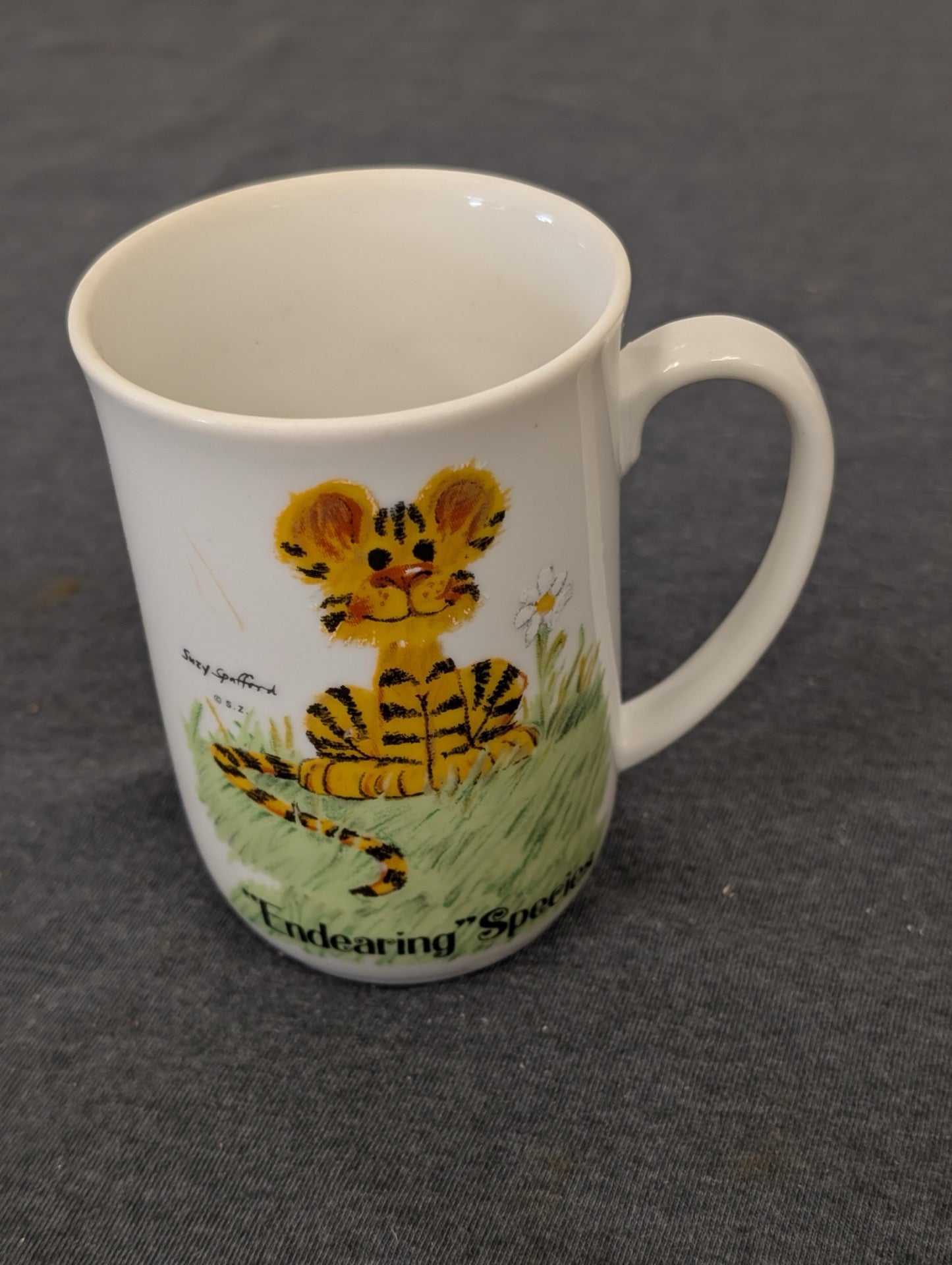 White ceramic mug showing an illustration of a cute tiger cub sitting in grass by Suzy Spafford.
