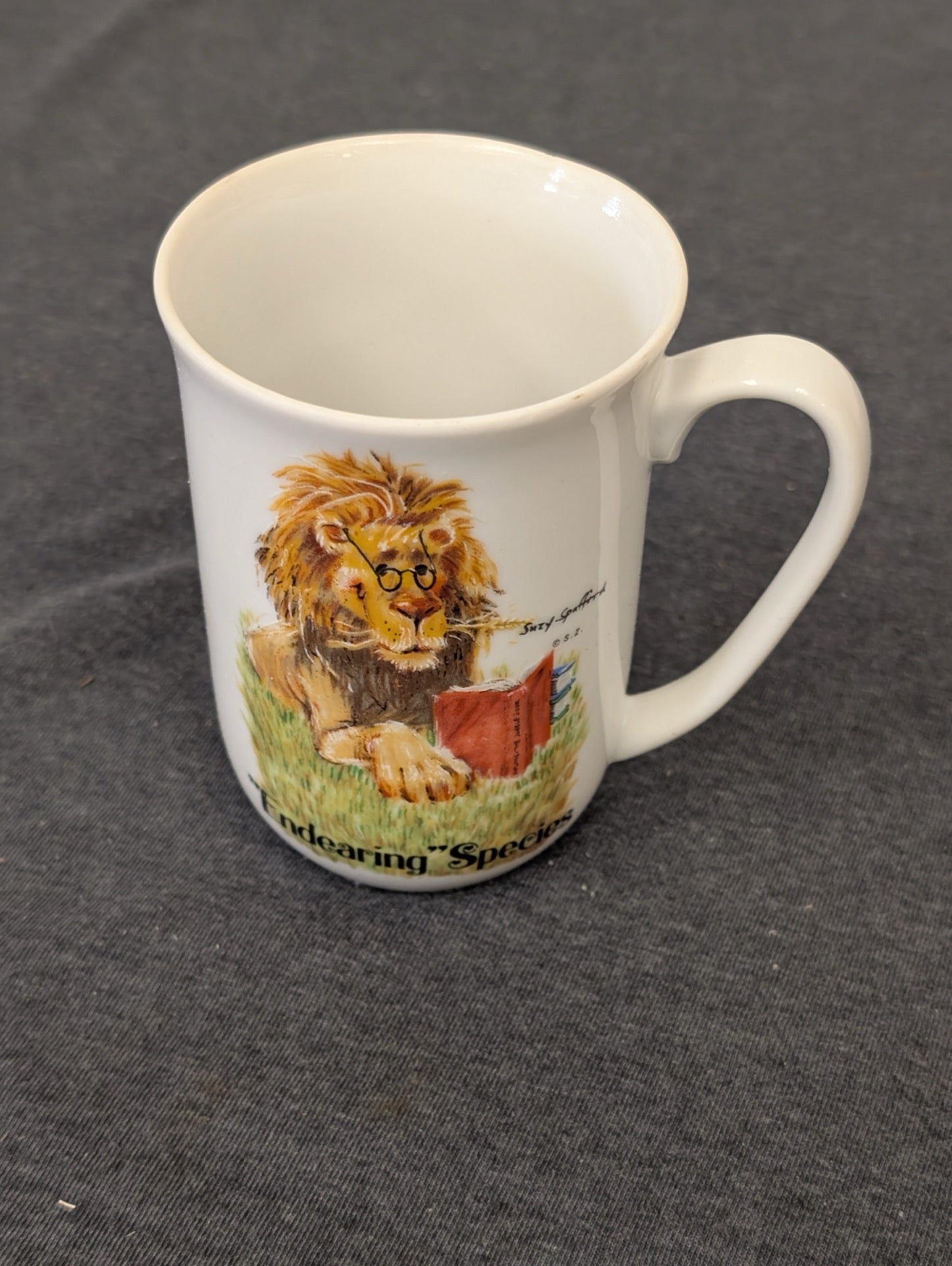 White coffee mug featuring an illustration of a lion wearing glasses and reading a book by Suzy Spafford.