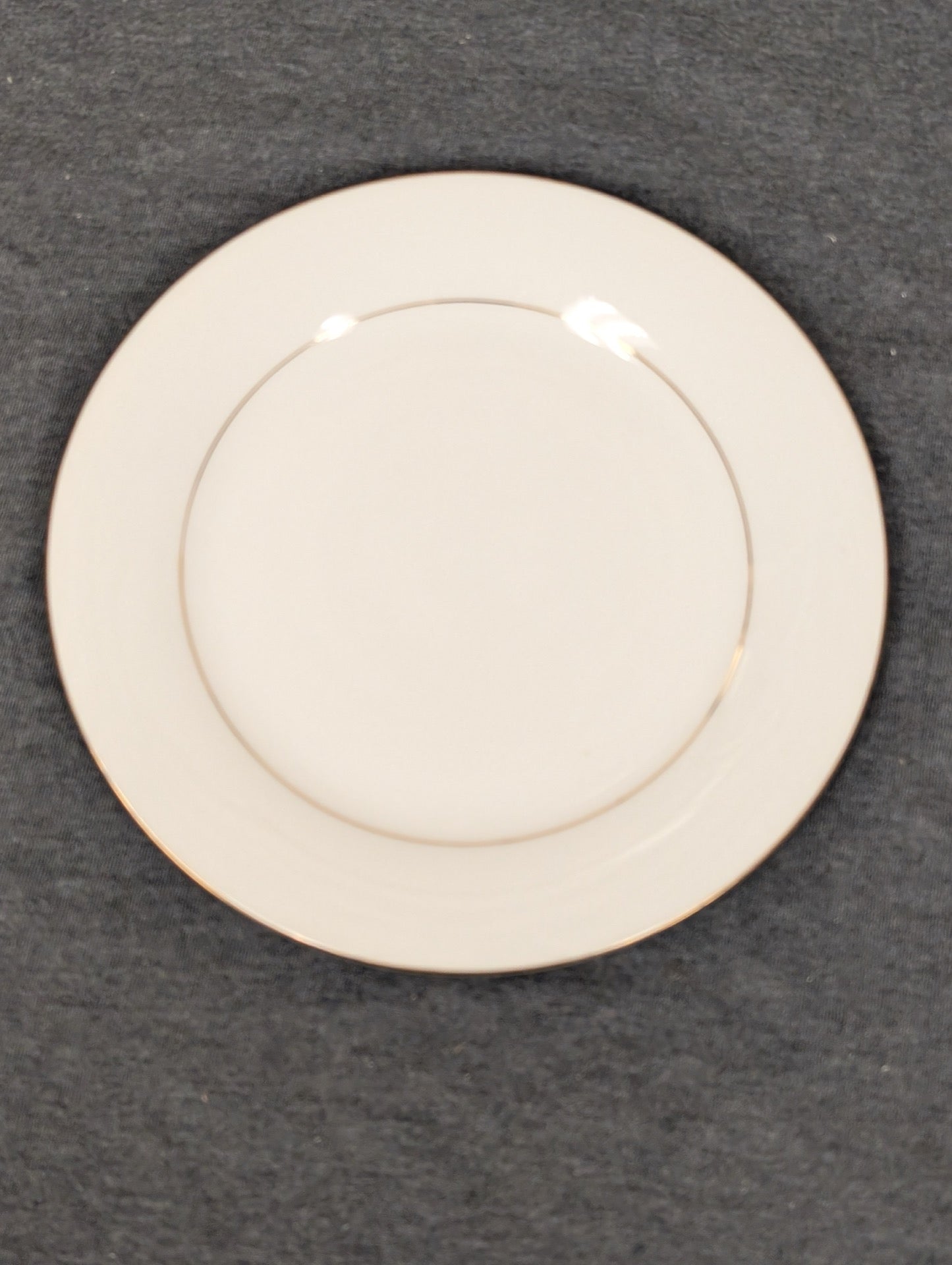 Front view of a white Sakura Classic Gold dinner plate with a gold band.