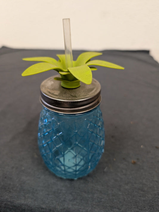 Blue textured glass mason jar shaped like a pineapple with a green leafy lid and straw