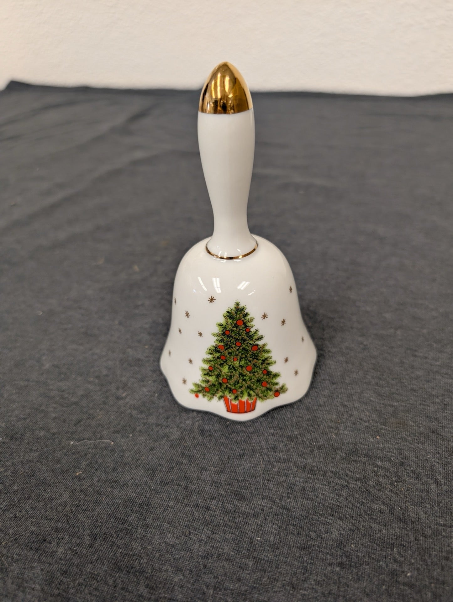 White ceramic bell with a painted Christmas tree motif and a gold-painted handle.