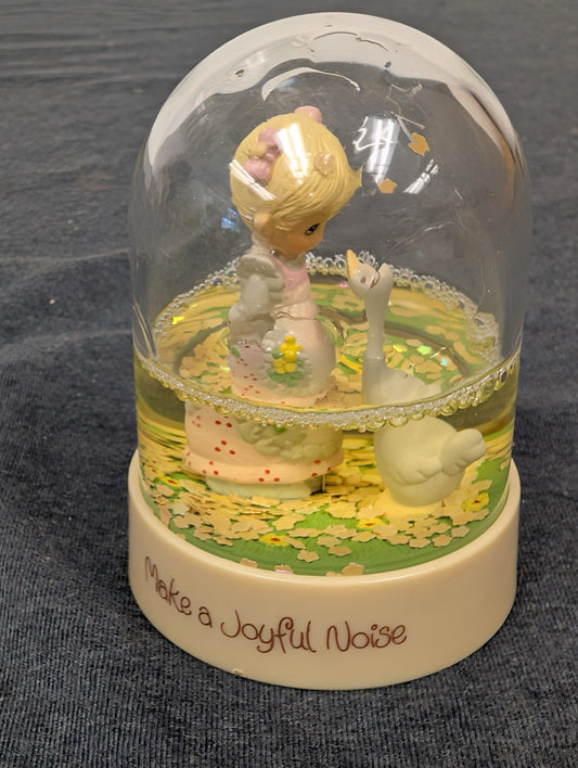 Precious Moments snow globe featuring a girl in a pink dress looking at a white goose, yellowing water.
