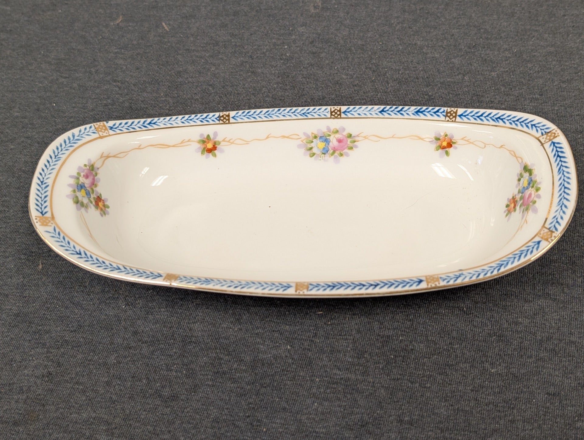 Elongated white porcelain dish with a blue and gold geometric border and small floral accents.