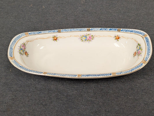 Elongated white porcelain dish with a blue and gold geometric border and small floral accents.