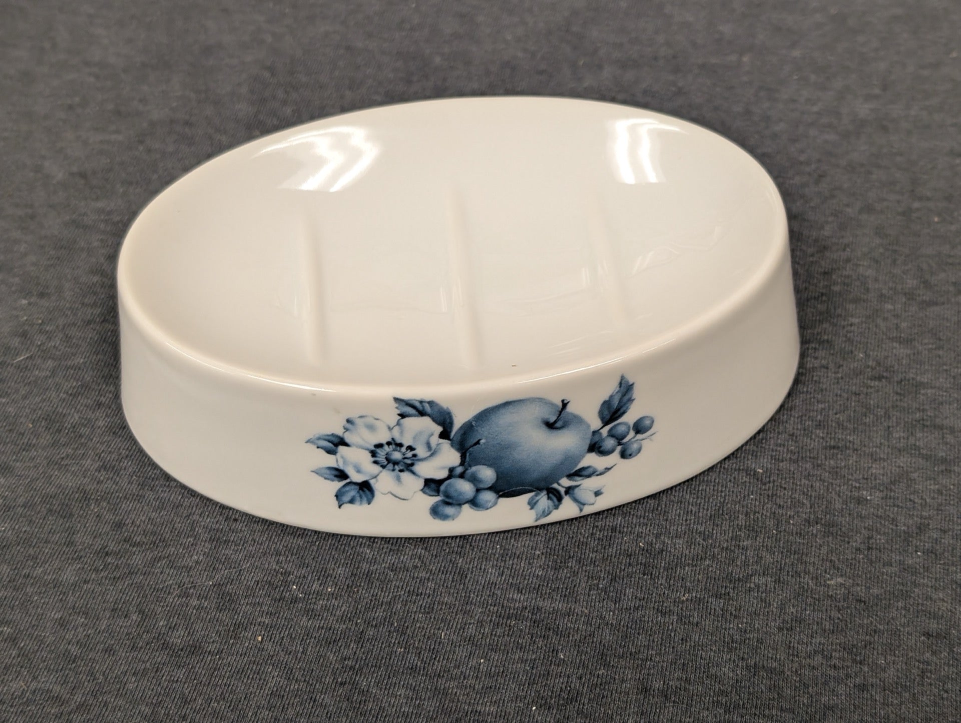 White ceramic soap dish featuring a blue apple and floral illustration.