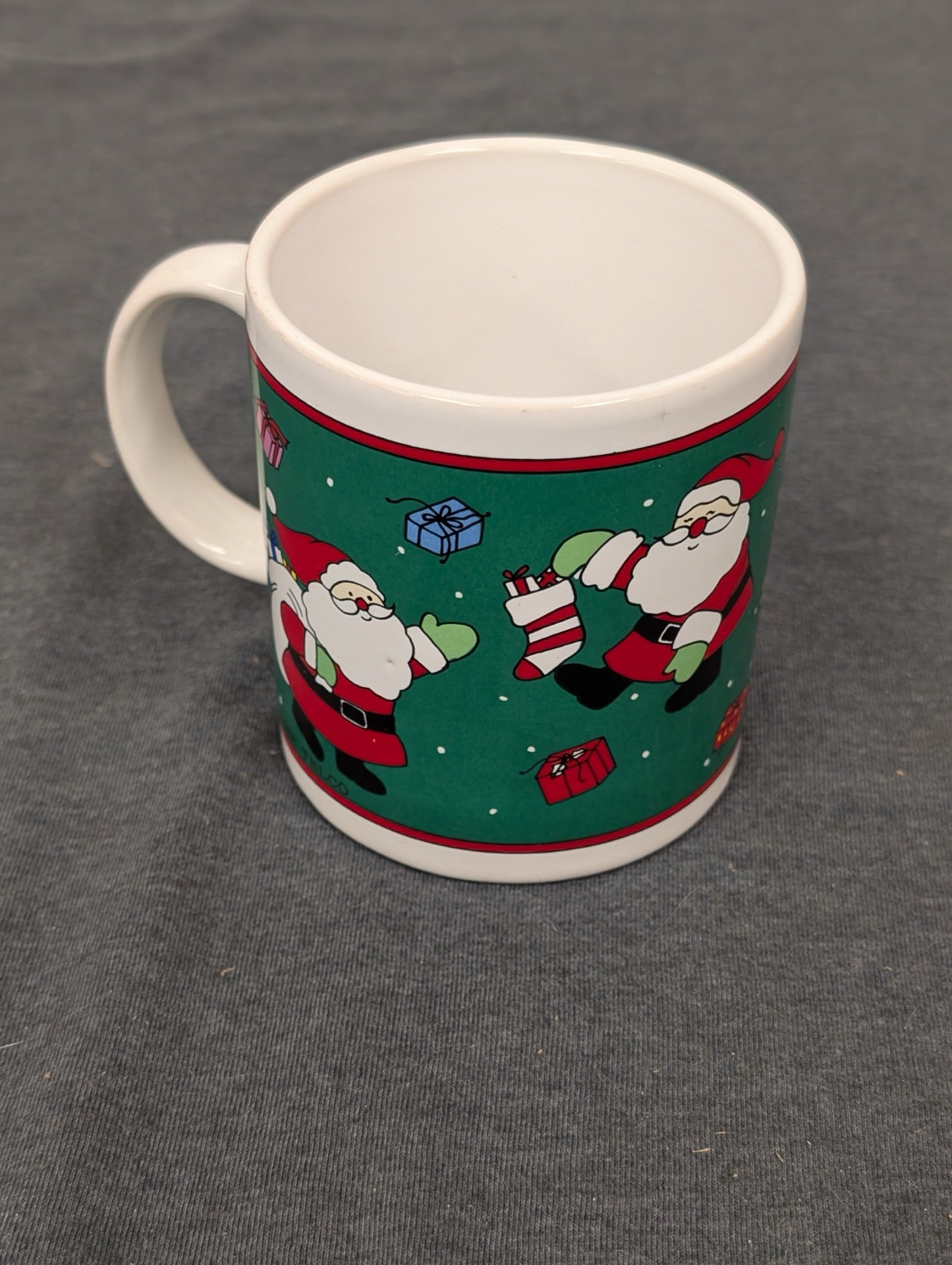 Ceramic coffee mug featuring a green background with Santa Claus and presents.