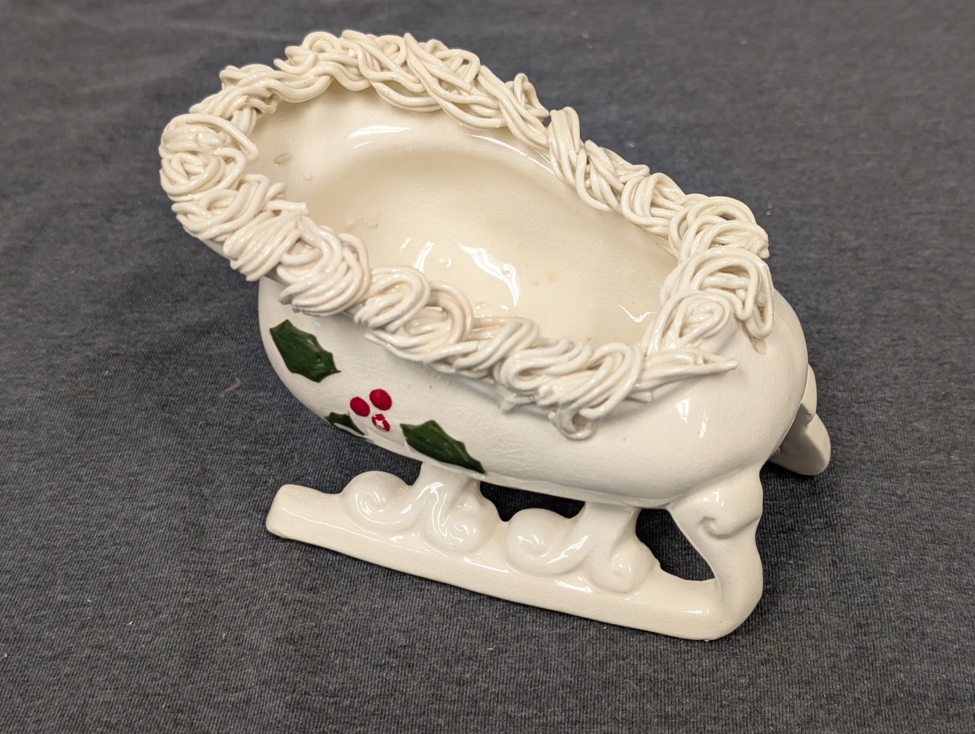 White ceramic sleigh planter decorated with holly leaves and textured white rim.