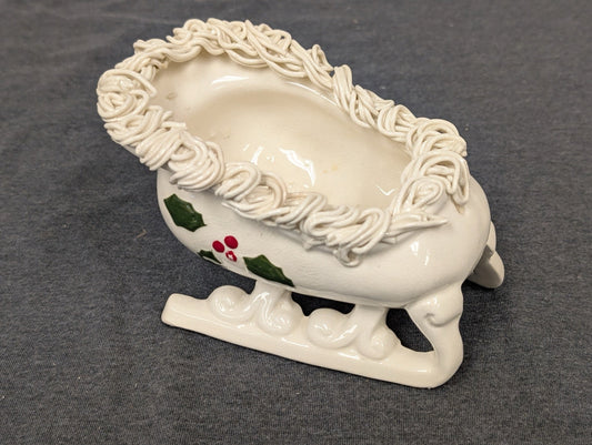 White ceramic sleigh planter decorated with holly leaves and textured white rim.