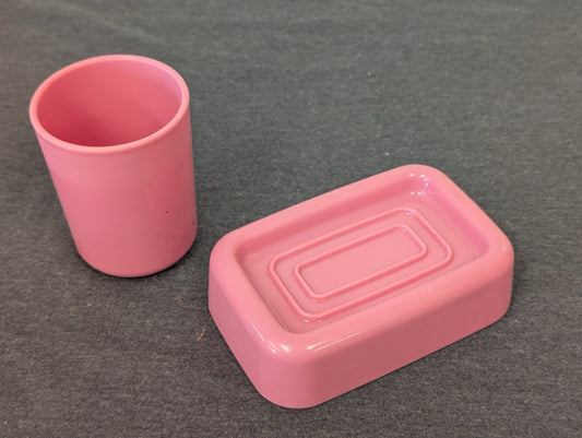 Pink plastic cup and rectangular soap dish on grey background