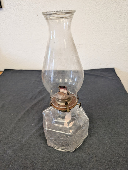 Clear glass oil lamp with a tall glass chimney on a dark table