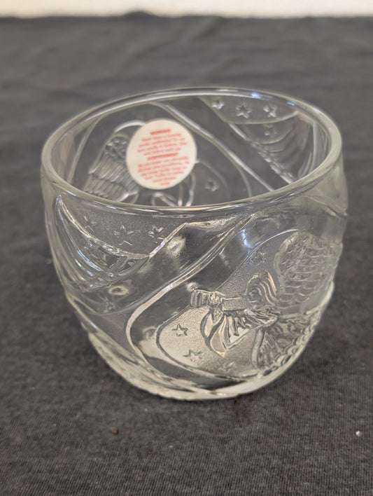 Clear glass votive holder with angel and star patterns, safety warning visible