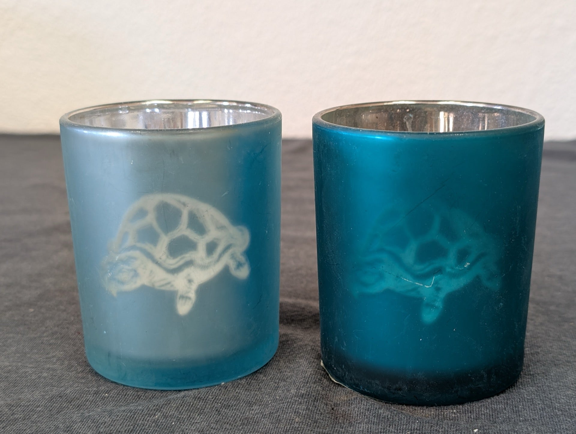 Two frosted glass votive candle holders with sea turtle design in dark and light blue