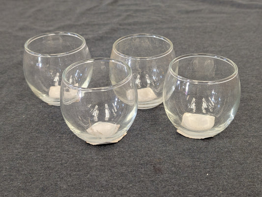 Set of four small round clear glass votive holders on a grey background