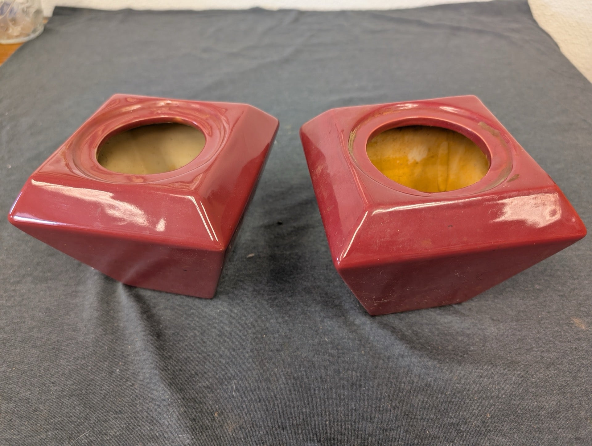 Two red ceramic square holders with a tapered shape and circular top opening