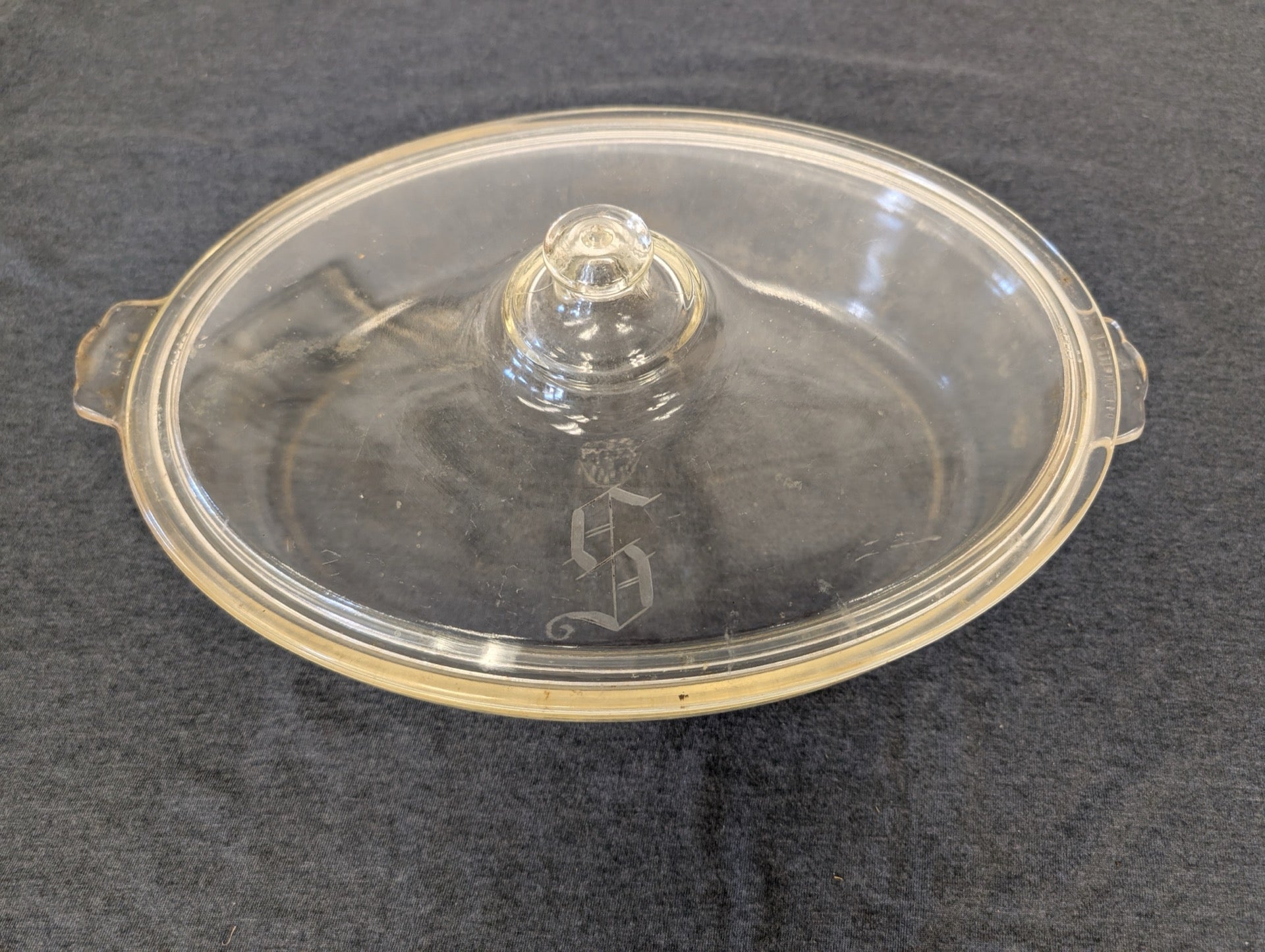 Clear glass oval casserole dish lid with an ornate letter S etched in the middle