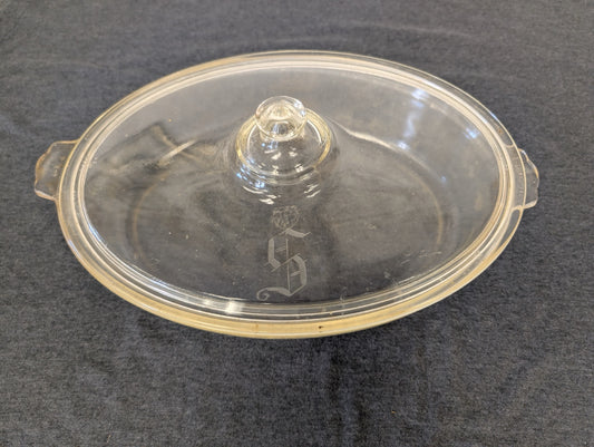 Clear glass oval casserole dish lid with an ornate letter S etched in the middle