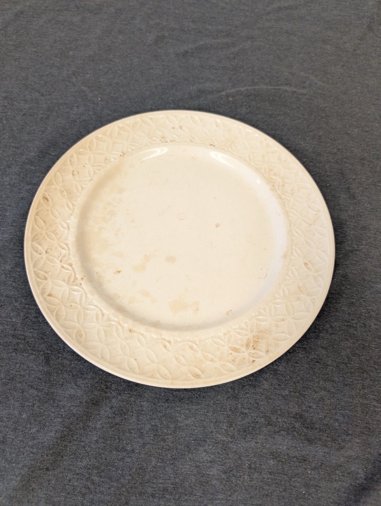 Cream plate with geometric rim pattern showing brown age spots and stains.