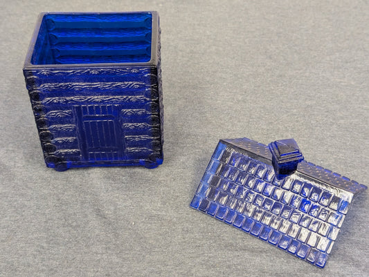Open cobalt blue glass box shaped like a log cabin with lid beside it.