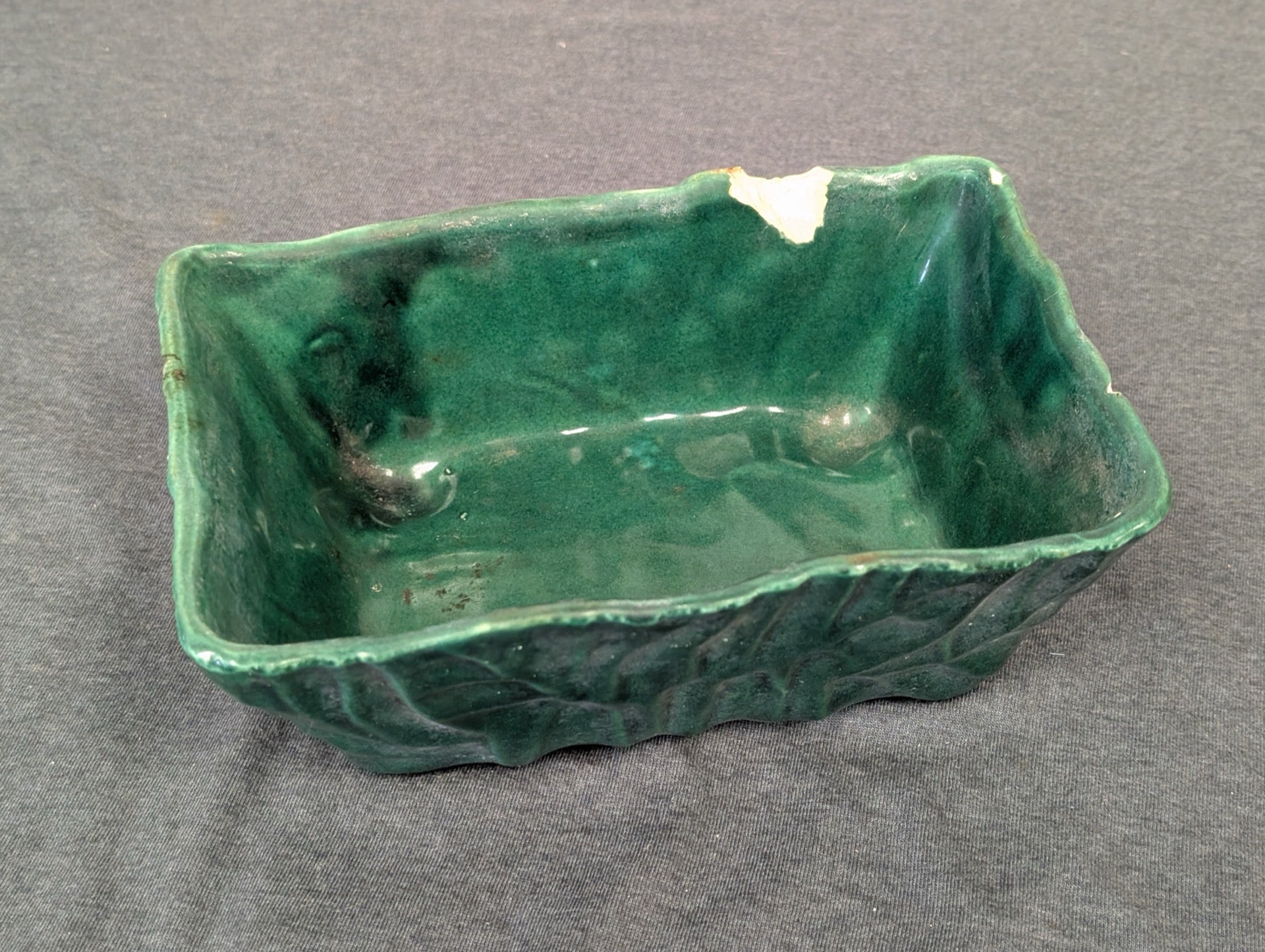 Green rectangular ceramic planter with leaf pattern and a large broken chip on the rim.