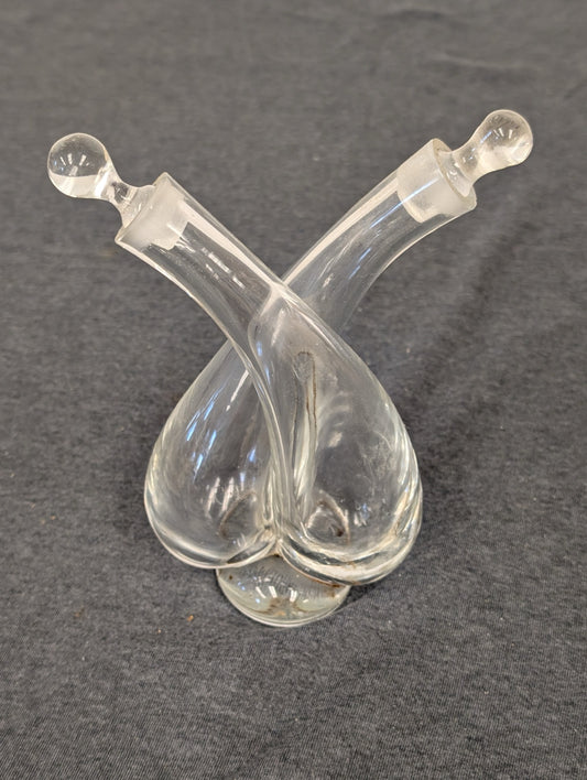 Clear glass double cruet with criss-crossing necks and two glass stoppers.